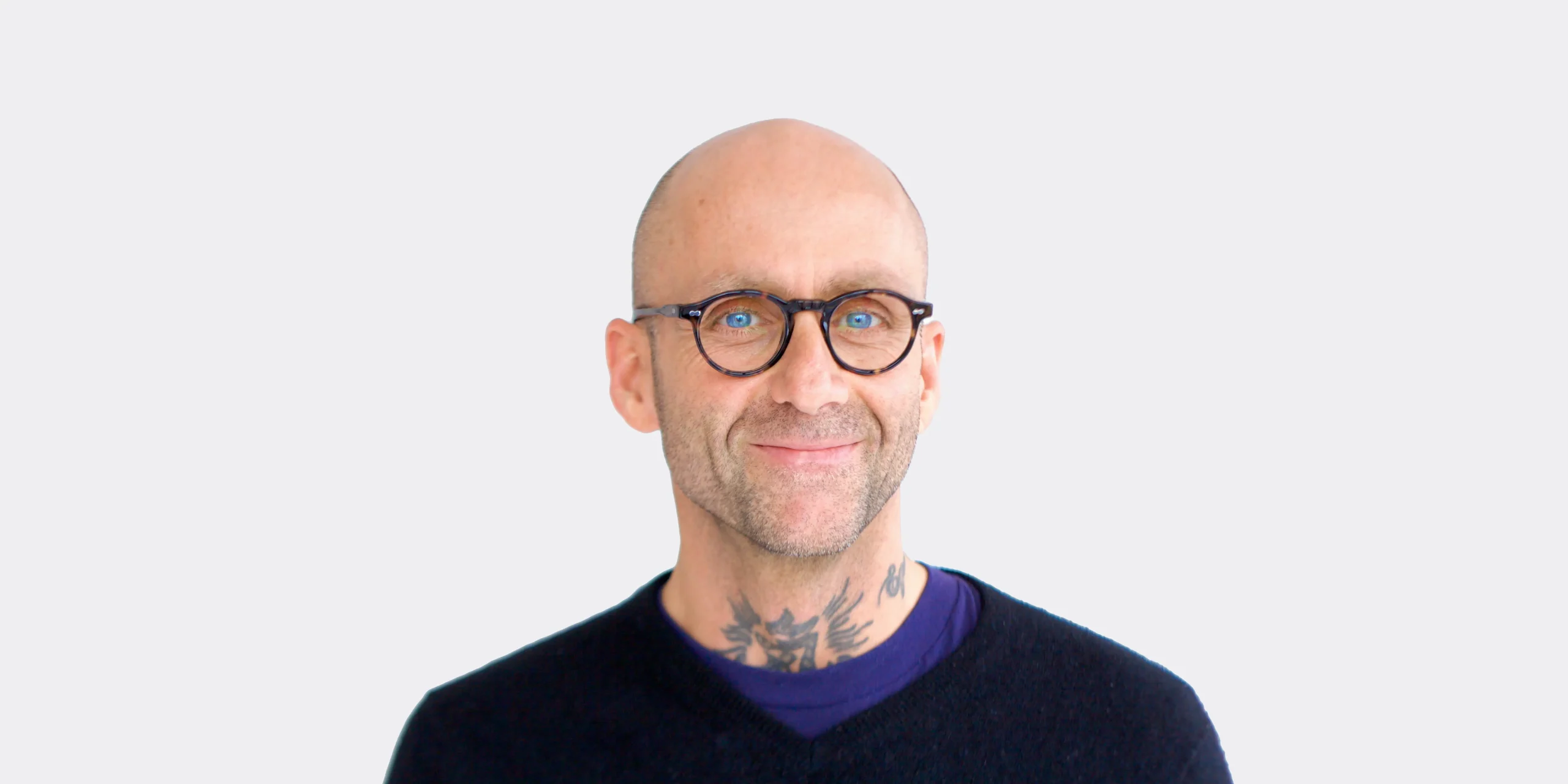 Biography photograph of Patrick Oancia smiling on a white background. Patrick is slim in this photo with a shaved head and looks quite relaxed.