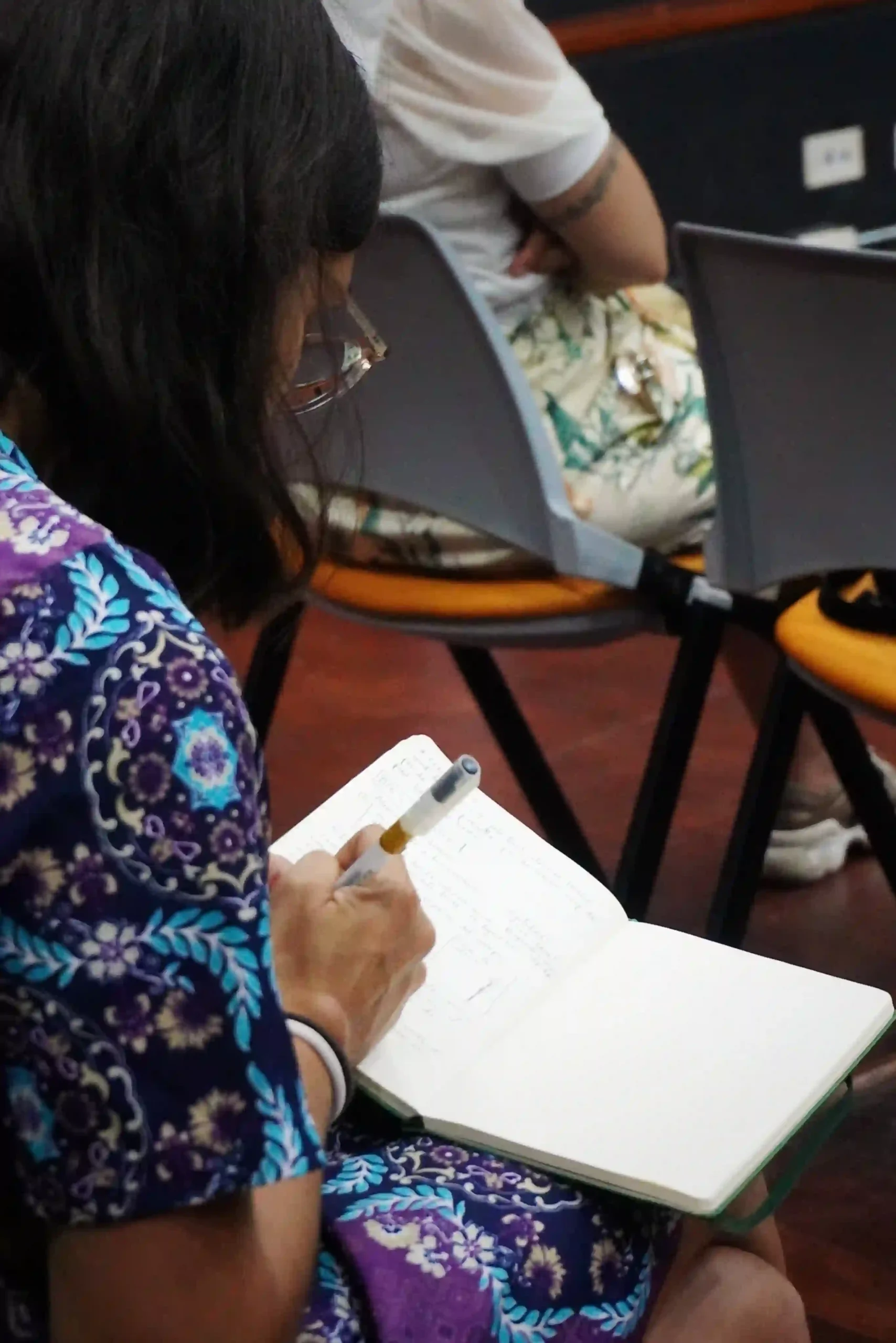 A woman wearing glasses and a dress with colourful patterns is taking notes