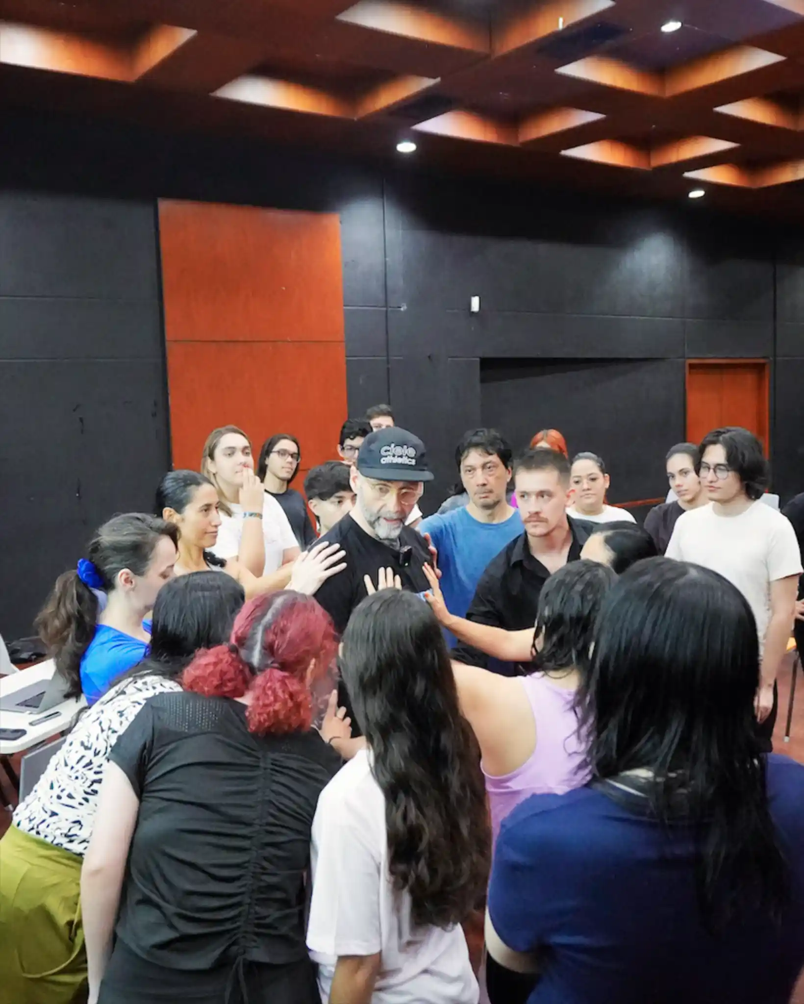 A group of students surrounding the instructor touching his body while he is demonstrating small movements.