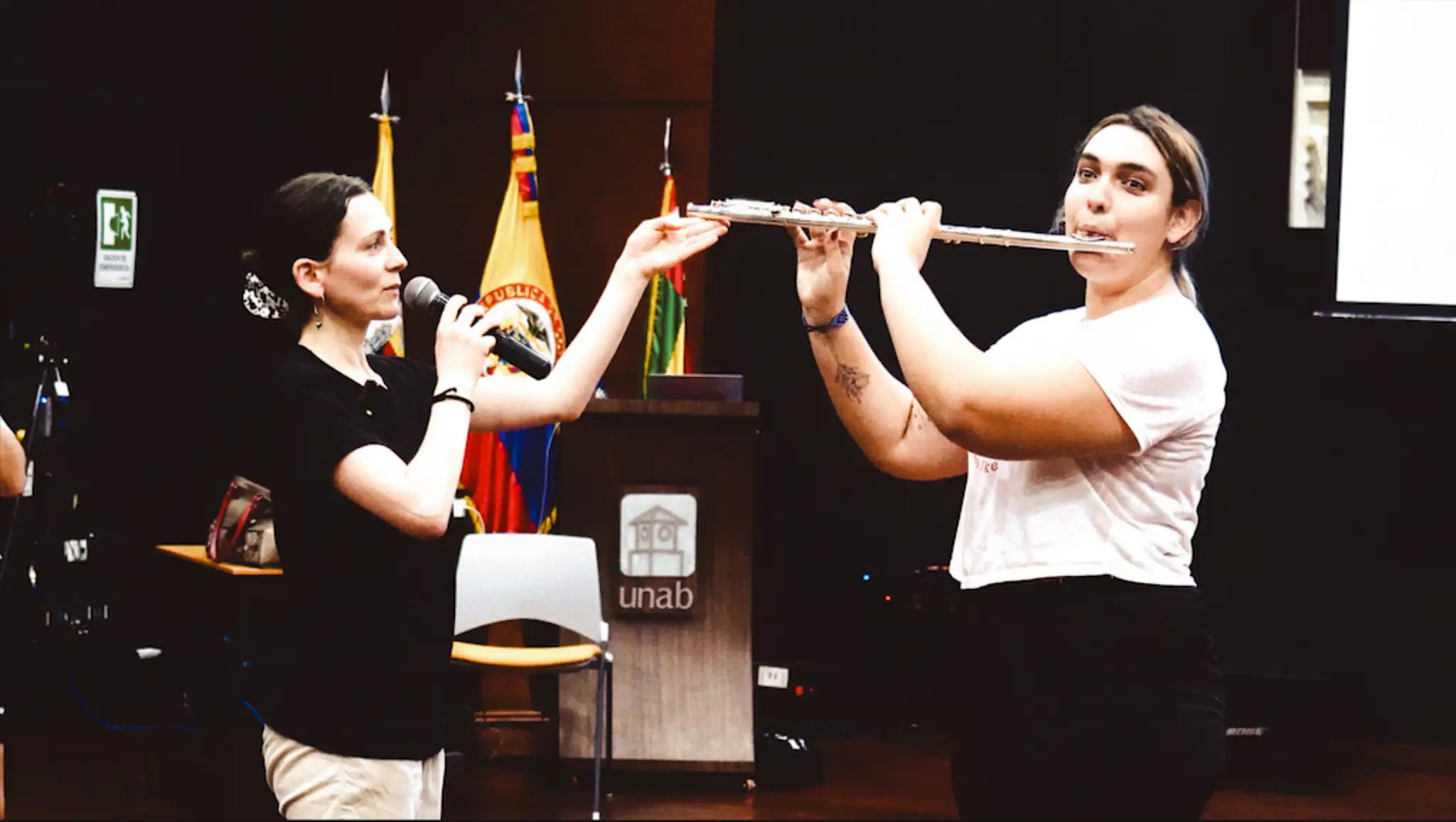 A student playing the flute happily while the instructor assists her with some advice on posture and body awareness.