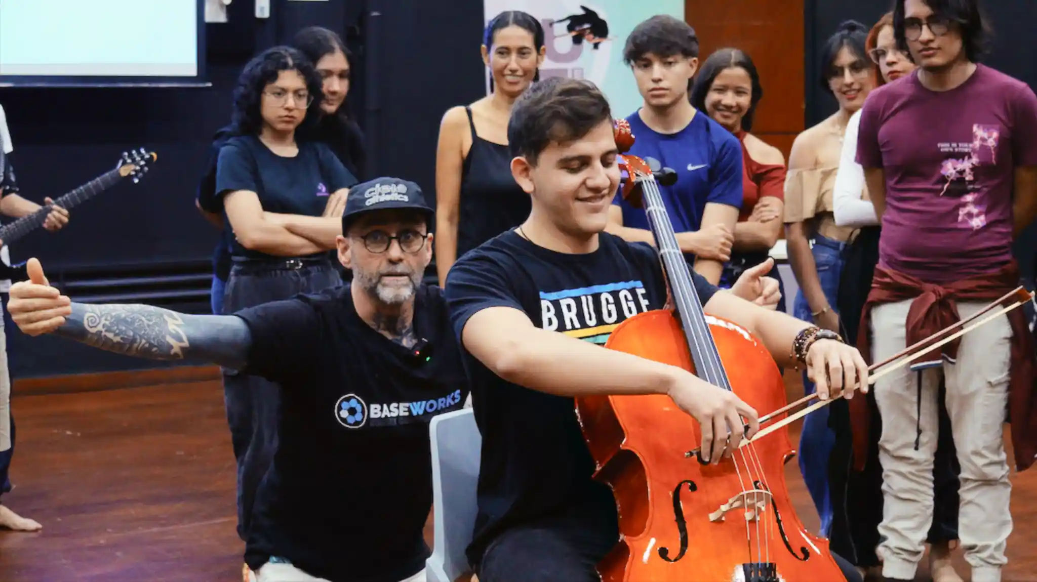 A music student playing the cello happily while the instructor demonstrates to the other students what to notice in the movement