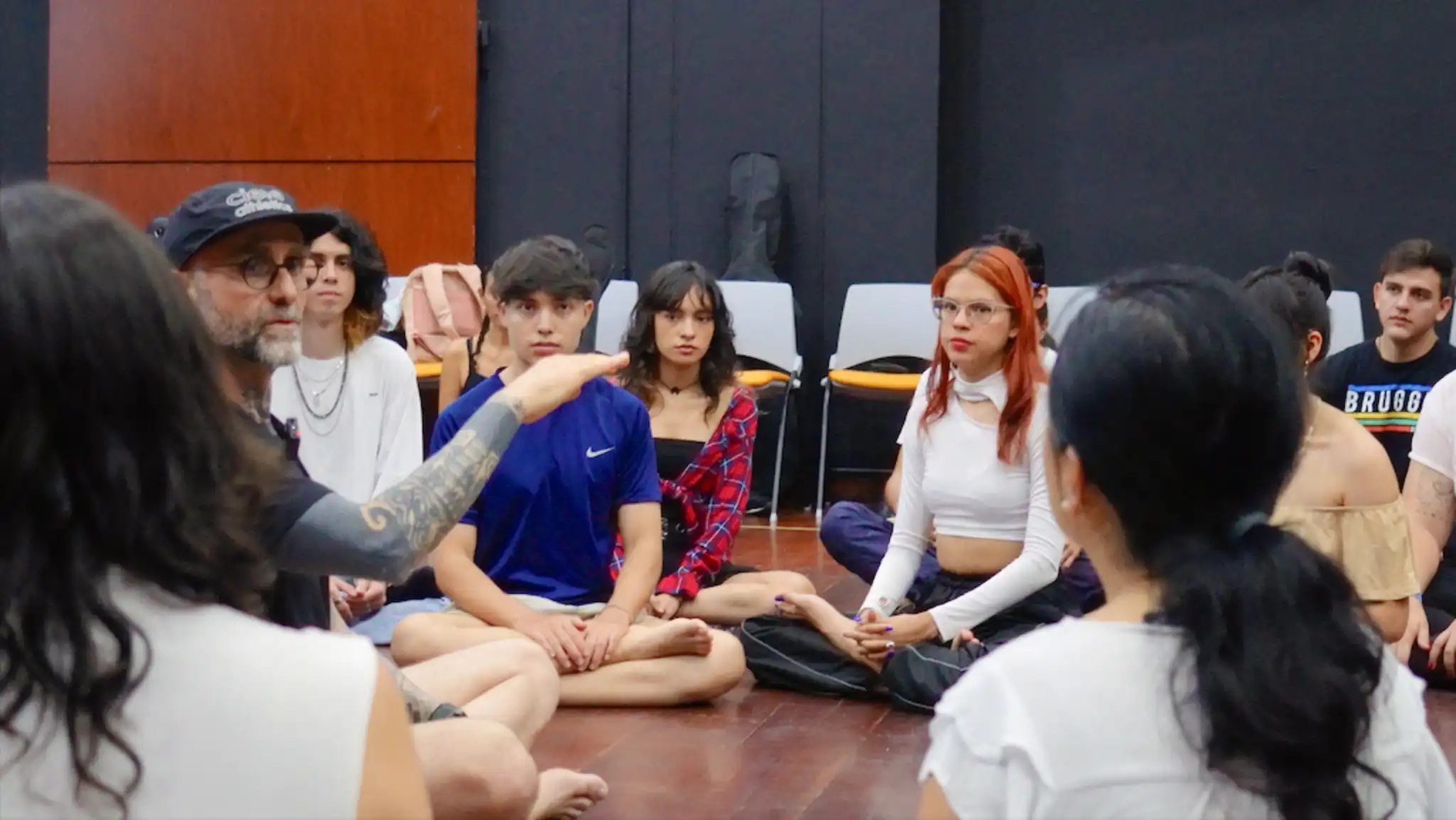 The instructor and music students sitting on the floor while the instructor explains a concept while the students listen intently