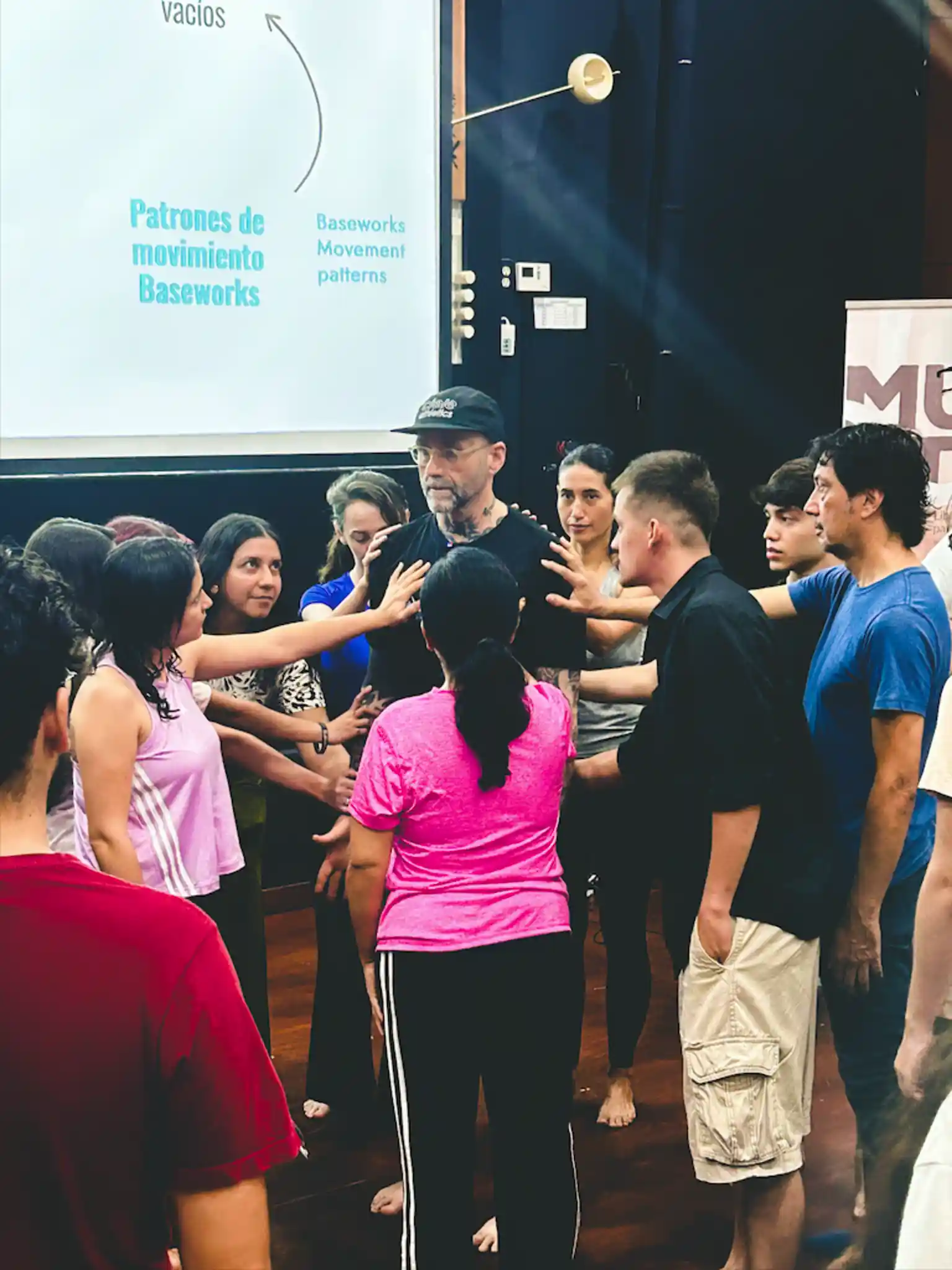 A group of students surrounding the instructor touching his body while he is demonstrating small movements.