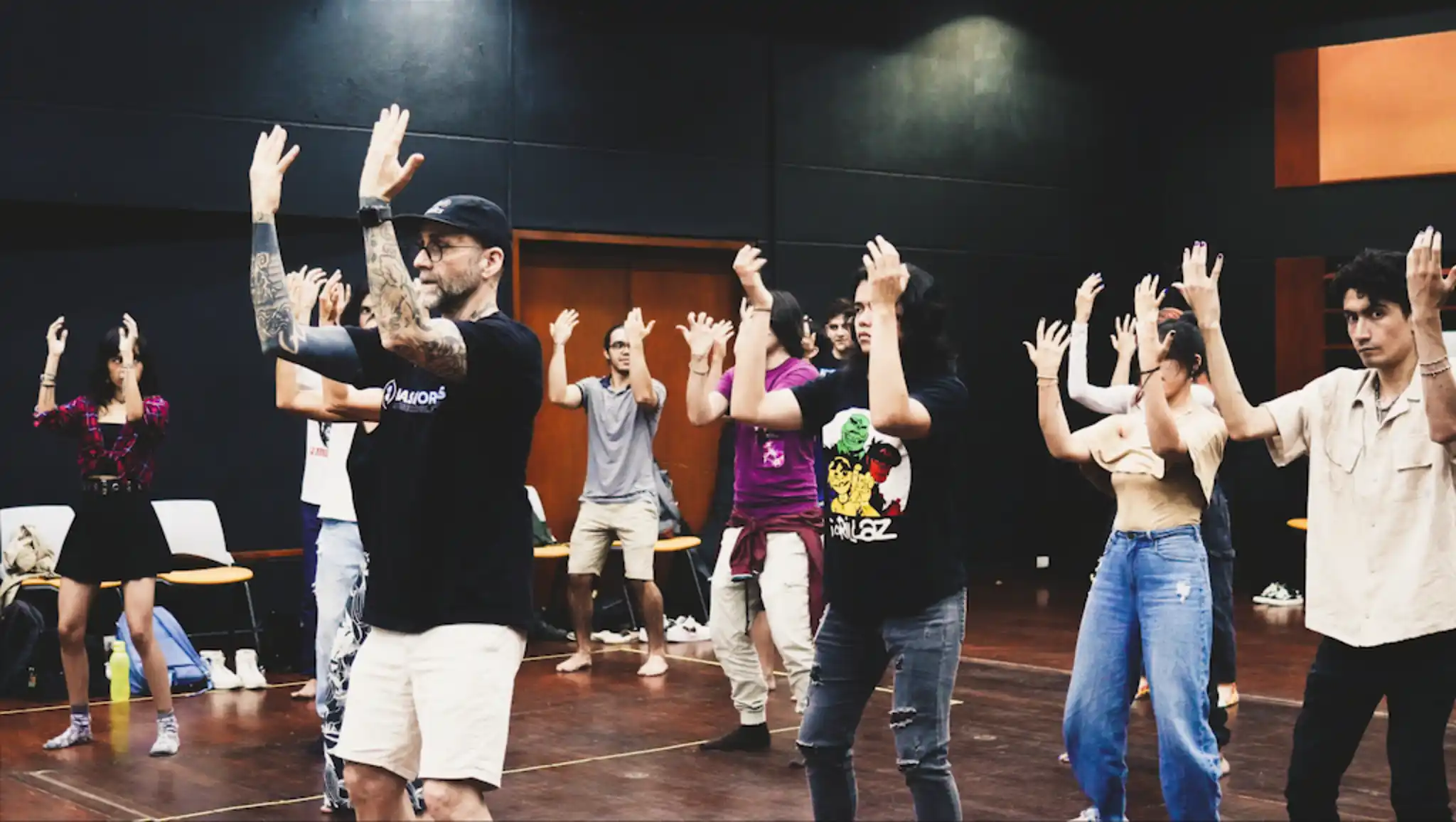 A group of students practicing a movement with the instructor demonstrating with their arms extended forward as they bend their knees slightly.