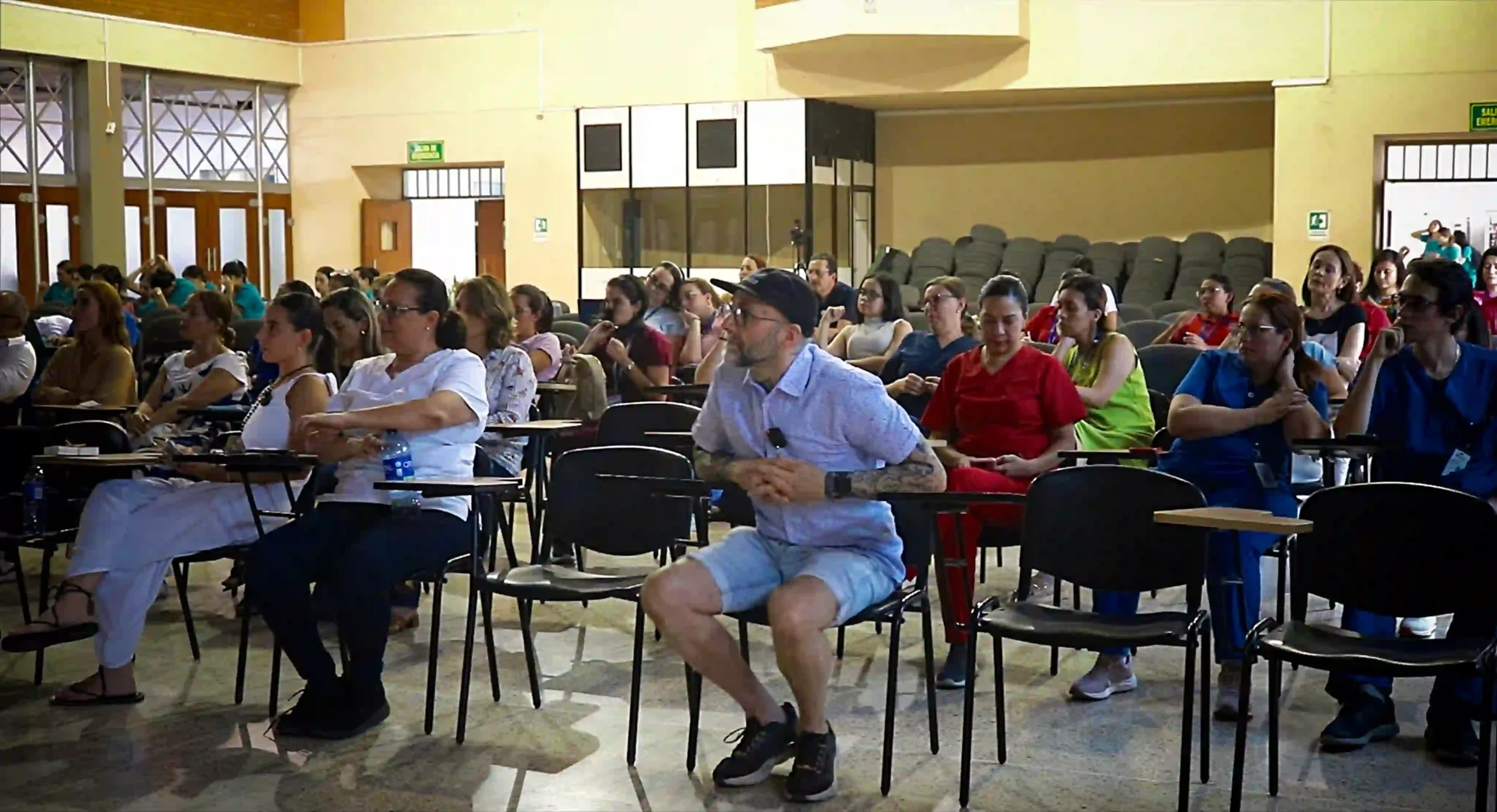 People, half of them dressed in medical uniforms, sit in a conference room intently listening to a presentation