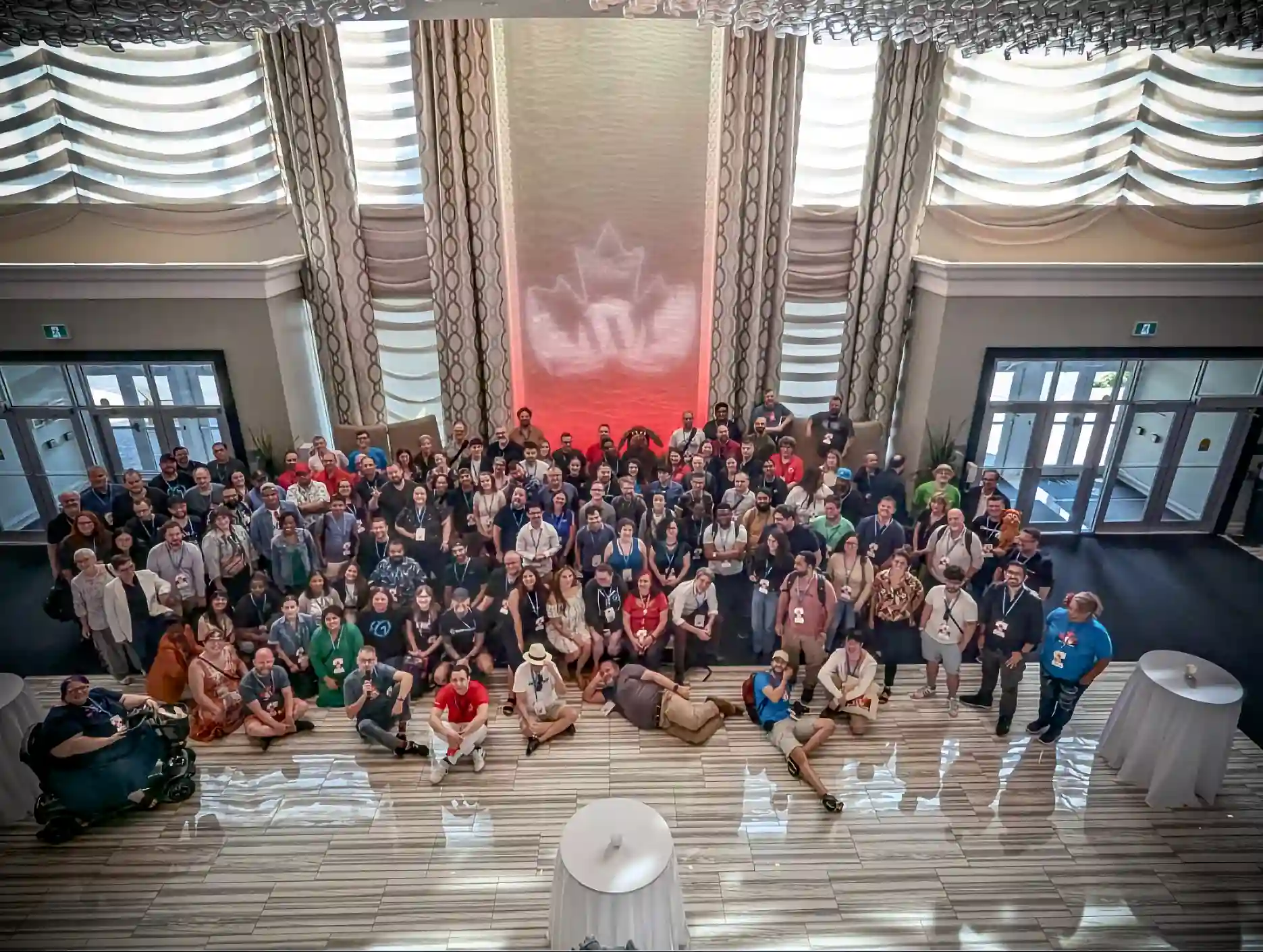 A group of about 125 people shot from above with a maple lead with a letter W inside it projected onto the wall behind. Photo taken at the end of WordCamp Canada 2024, a WordPress community event.