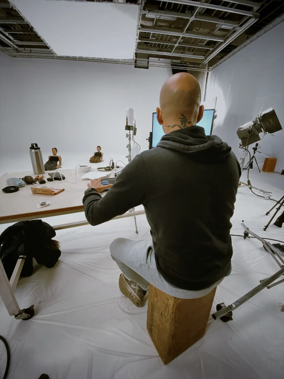 Patrick sitting on a wooden block editing in the studio with Satoko and Asia