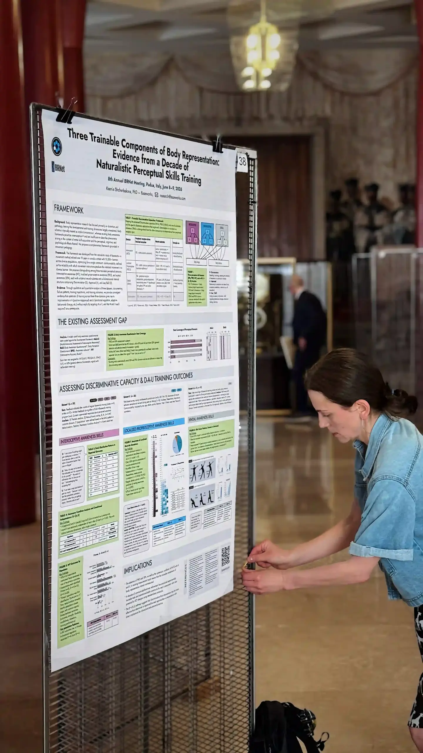 Ksenia Shcherbakova leans in to examine the Baseworks research poster mounted on a mesh display stand in the foyer of Palazzo del Bo, before the 8th Annual BRNet Meeting opens.