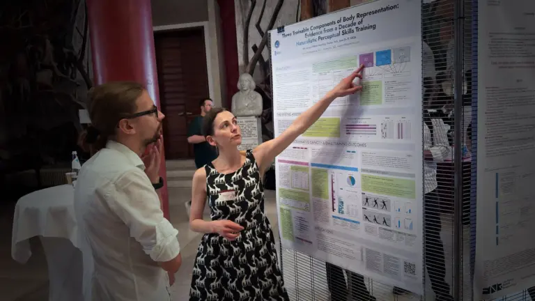 Asia (Ksenia) Shcherbakova pointing to a section of the Baseworks research poster in discussion with a conference attendee at BRNet 2026, Padova, Italy.