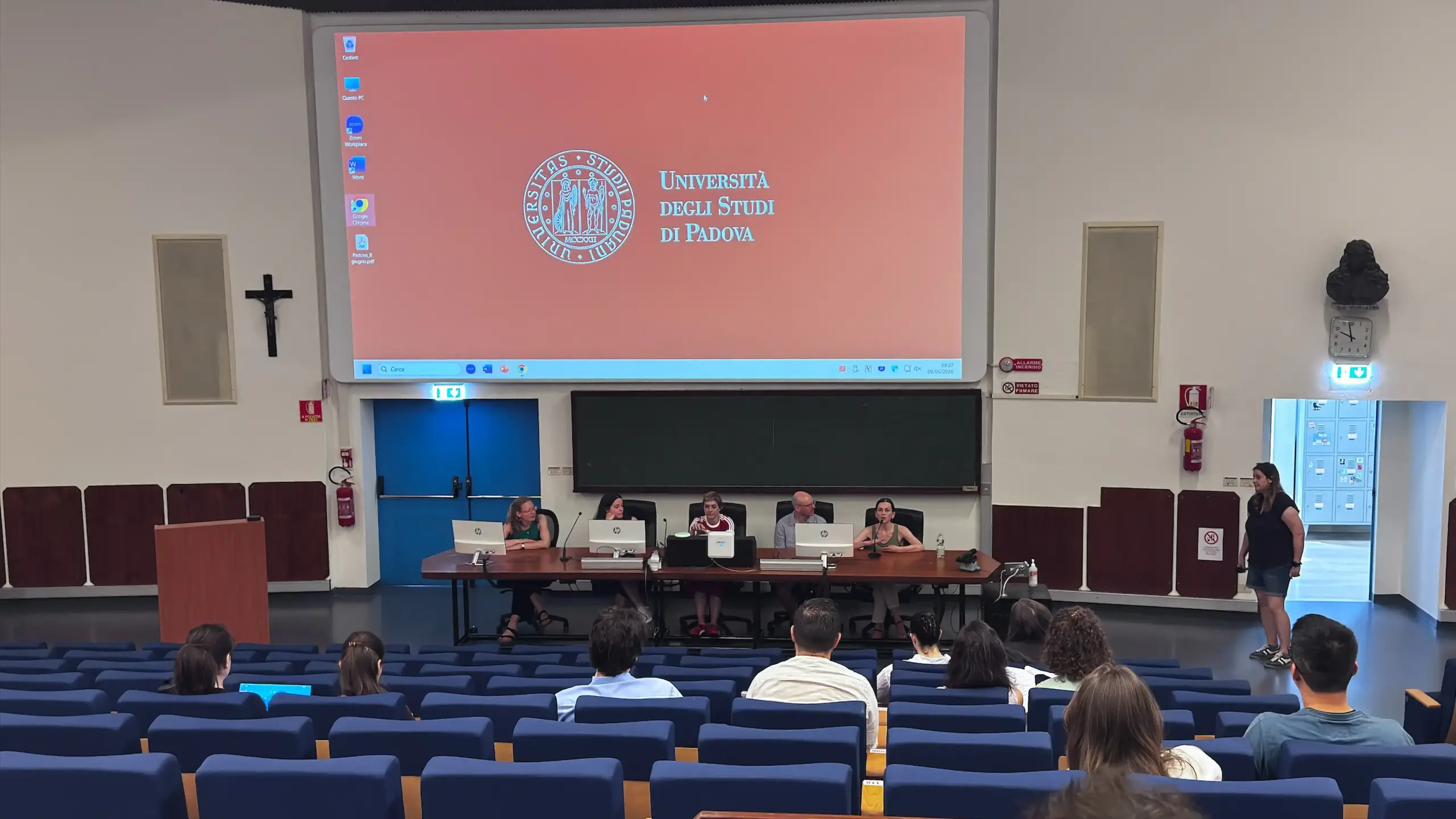 Four panelists seated at a long table at the front of a lecture auditorium for the early-career researcher panel at BRNet 2026. The screen behind them displays the Università degli Studi di Padova seal. Blue upholstered seating and audience visible in the foreground. Area Giustinianea, Day 2.