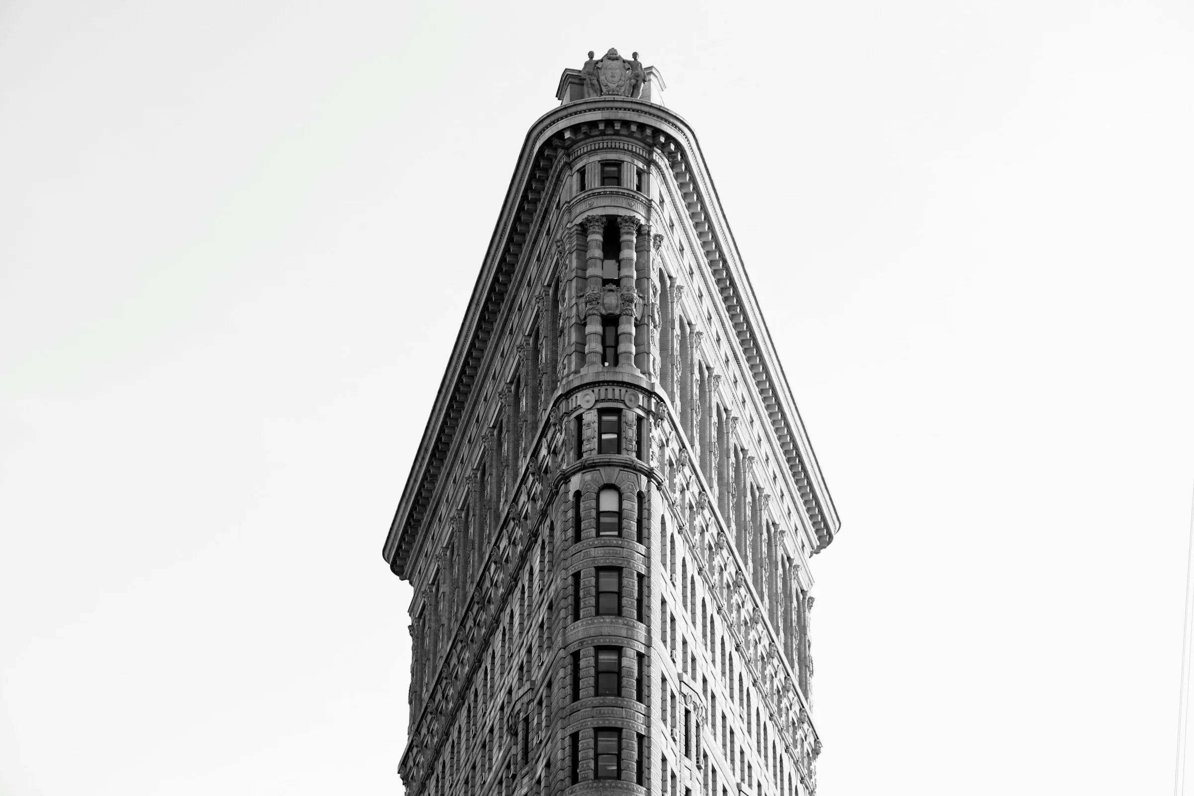 The Flatiron Building in New York City, viewed from street level against a bright sky, showing its narrow triangular facade.