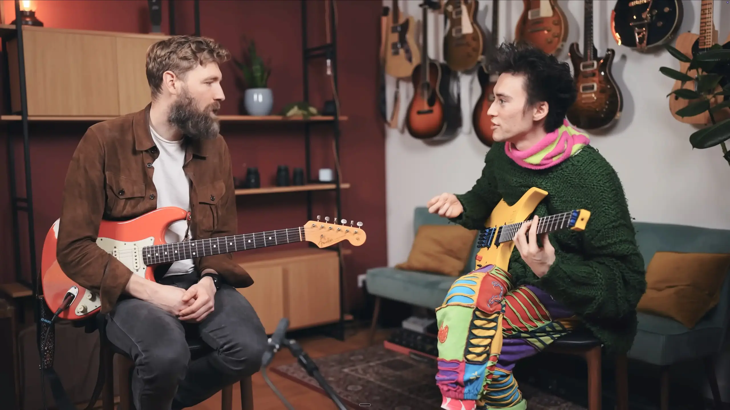 Jacob Collier and Paul Davids seated together with guitars during an interview about Collier's five-string guitar design.