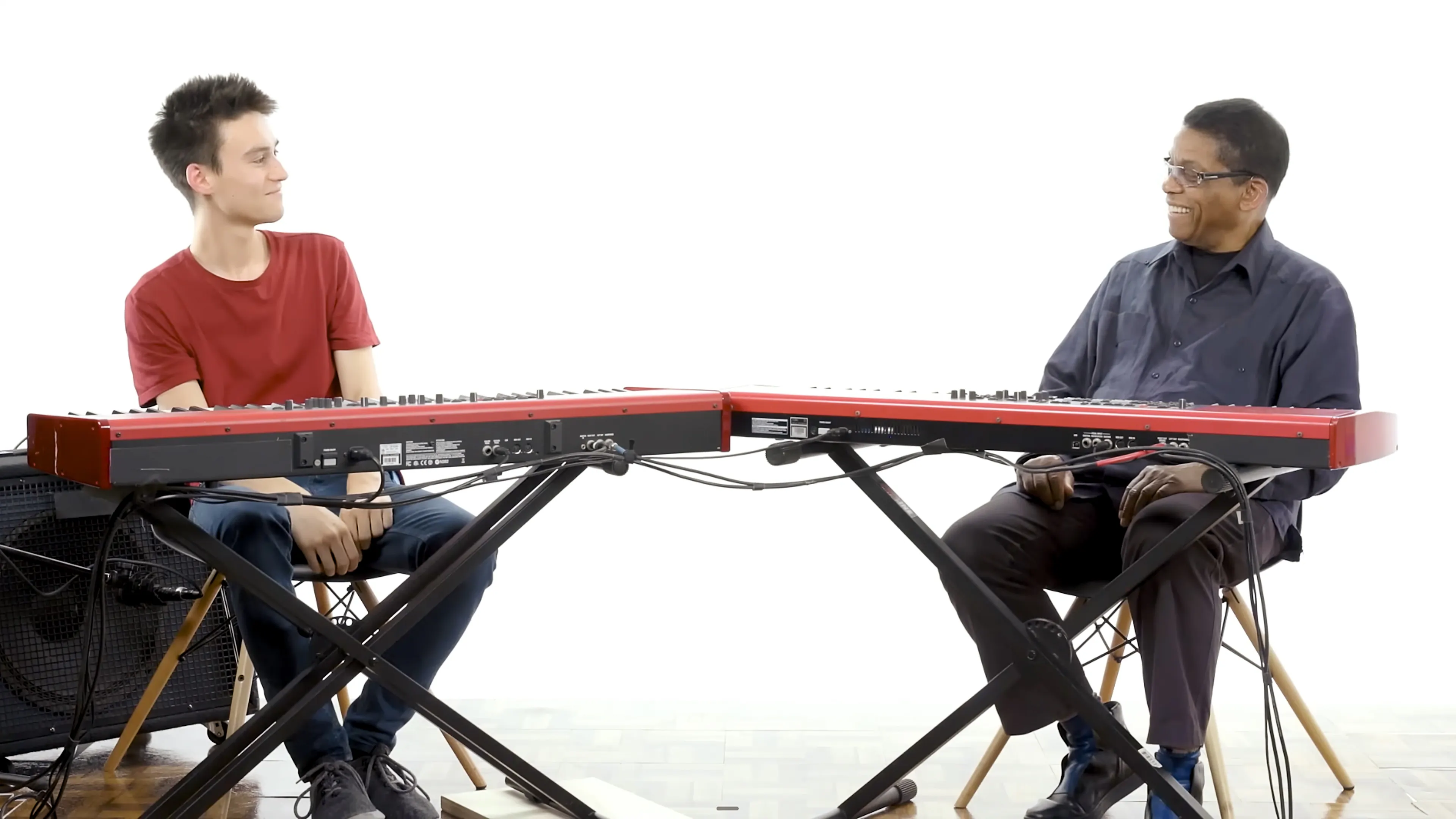 Jacob Collier and Herbie Hancock seated across from each other at connected keyboards during a conversation about harmony.