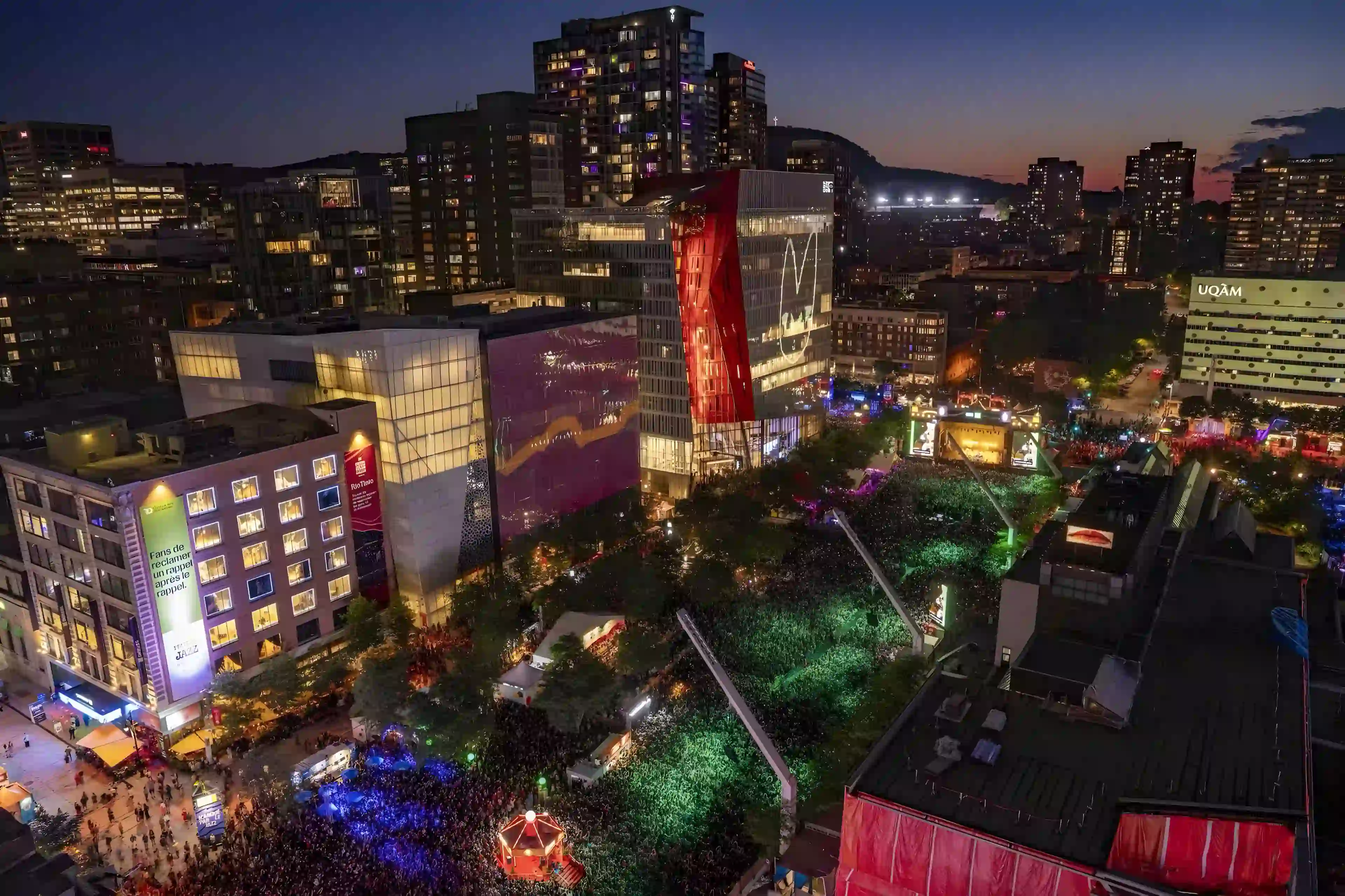 Aerial night view of the Montreal International Jazz Festival grounds and crowd during Angine de Poitrine's 2026 show.