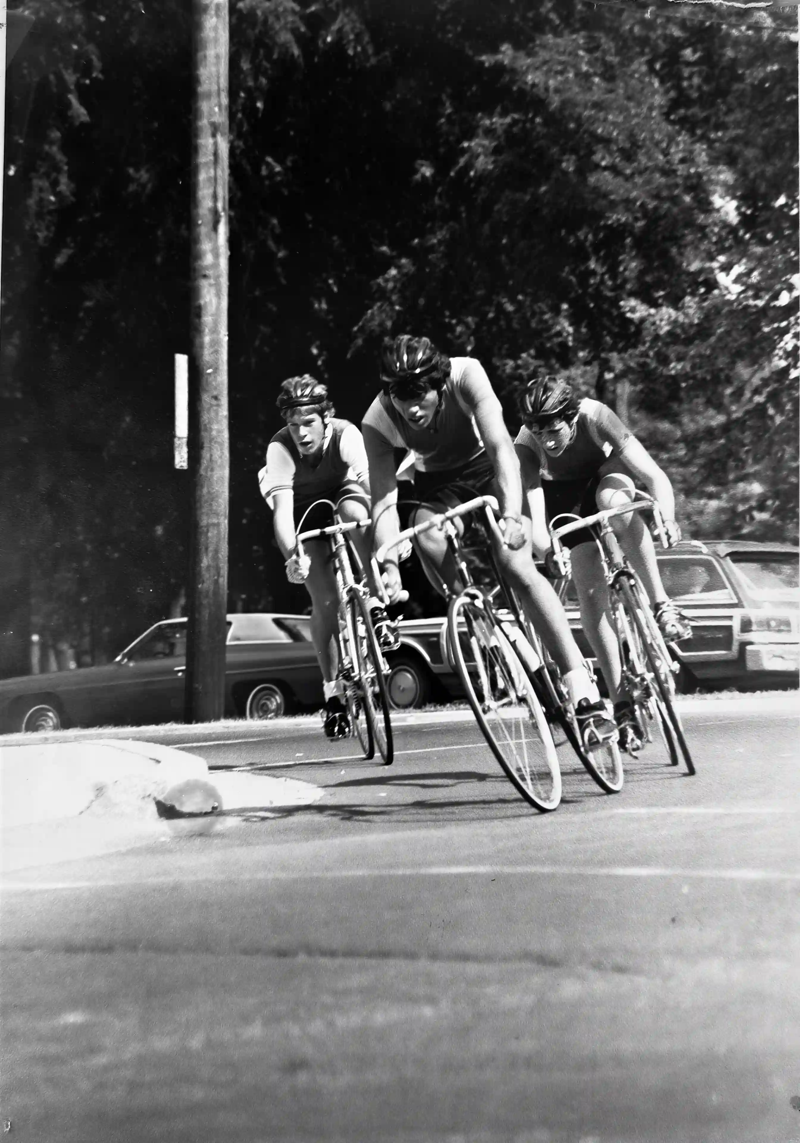 Patrick Oancia racing on a bicycle alongside two other cyclists on a tree-lined road in Halifax, Nova Scotia, 1979.