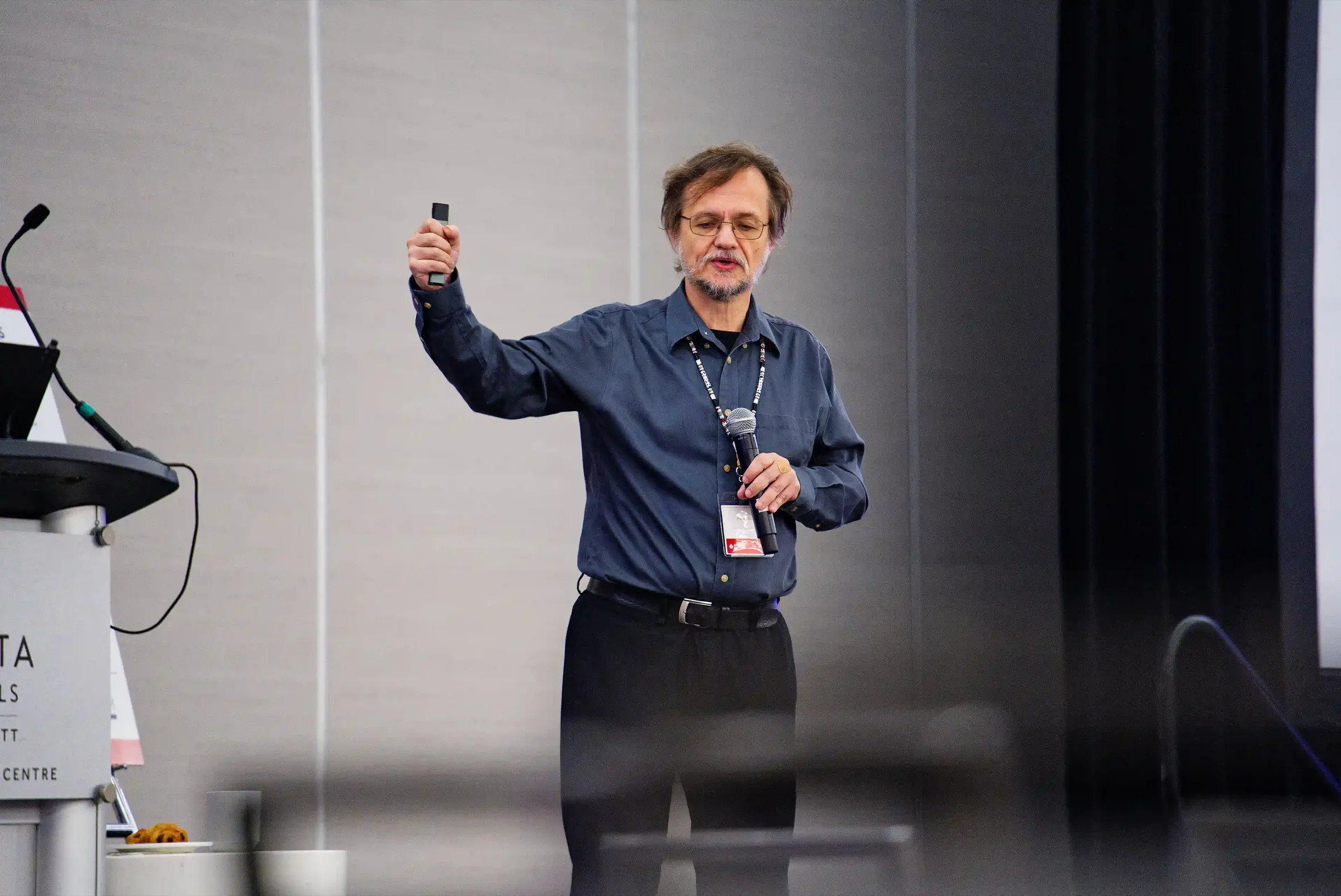 Dr. Paul Cisek holds up a presentation remote and a microphone while giving his keynote at SCAPPS 2026.