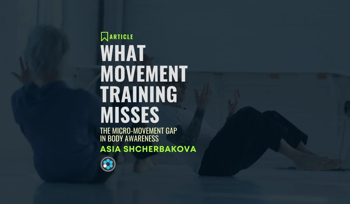 Two individuals seated on the floor doing slow, controlled movement exercises in a spacious studio.